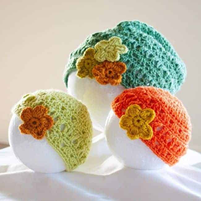 two lace crochet baby hats and one lace crochet adult hat all with decorative flowers attached