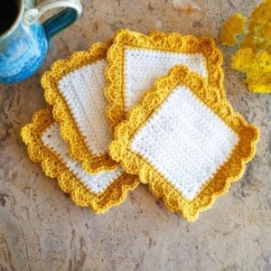 four white and yellow square crochet coasters next to mug and flowers