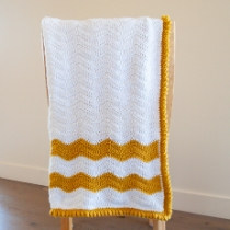 Yellow and white crochet baby blanket hanging over a chair