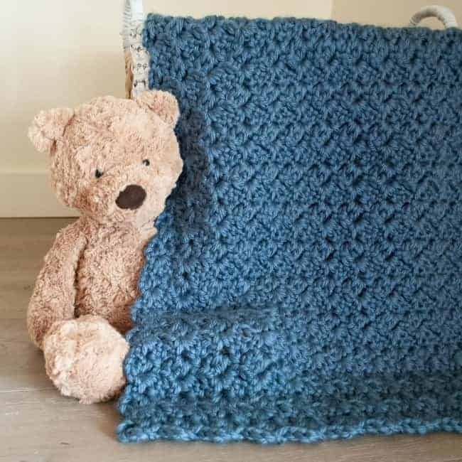 teddy bear sitting next to crochet baby afghan