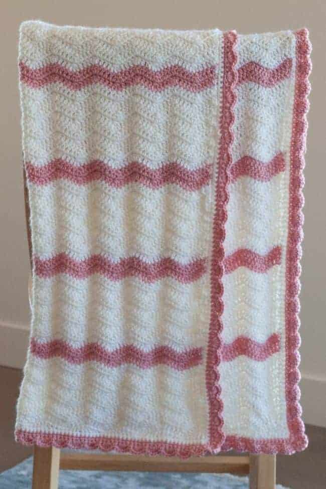 pink and white crochet baby blanket with shell border hanging over chair