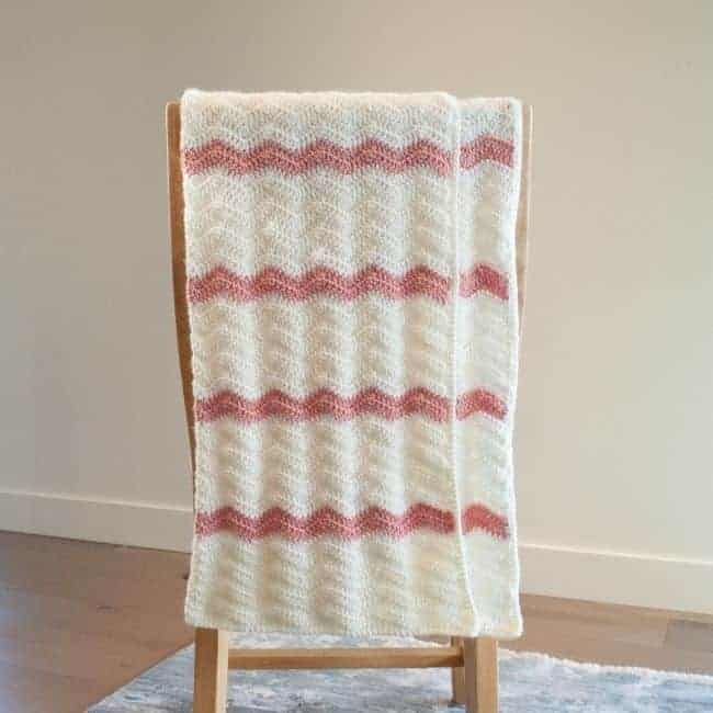 pink and white crochet baby blanket with smooth border folded over chair