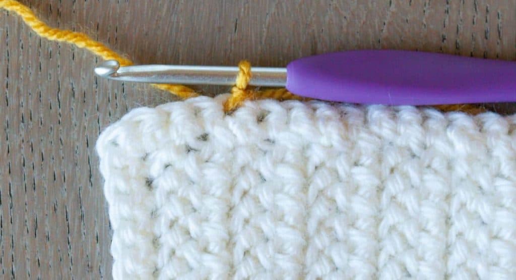 close up of white crochet square showing stitch placement of first stitch of yellow border