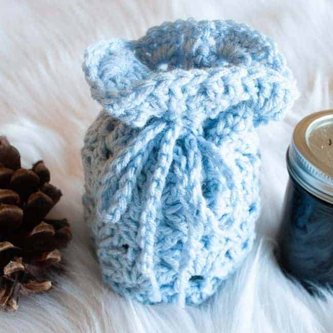 blue small crochet gift bag holding half pint mason jar and next to another half pint mason jar and a pine cone