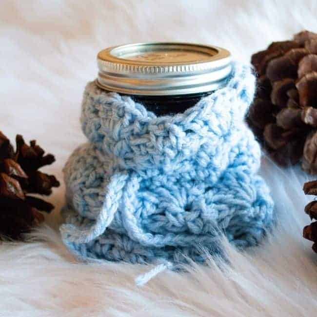 blue small crochet gift bag holding half pint mason jar and next to pine cones