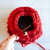 top of crochet hat with hole in it and tapestry needle beginning to weave it closed