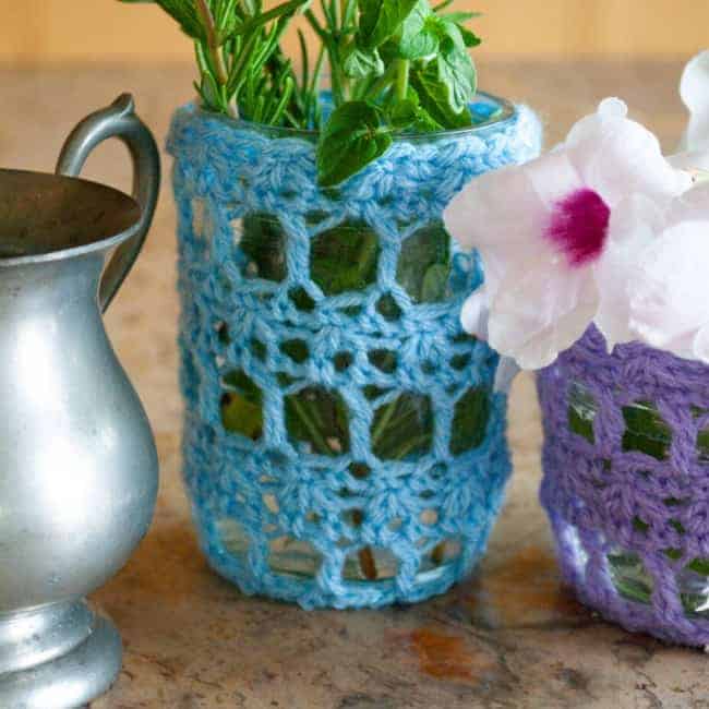light blue crochet mason jar cover over jar next to silver cup and part of purple jar cover