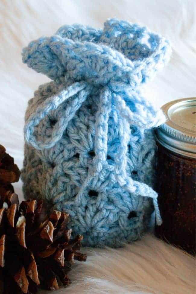 blue small crochet gift bag next to half pint jar of jam and pinecones