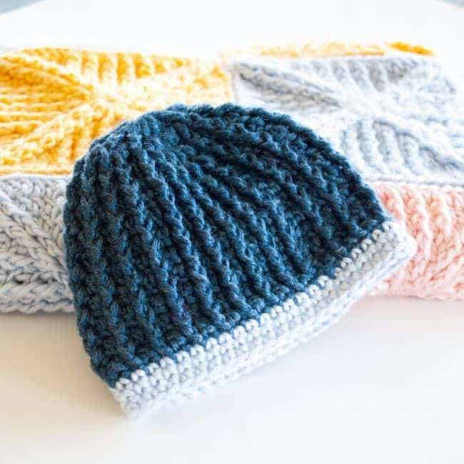 blue crochet baby hat in front of a folded crochet baby blanket