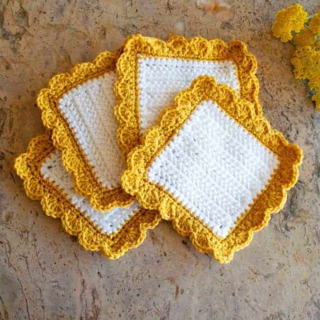 four white square crochet coasters with yellow shell border