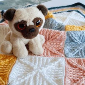 stuffed puppy dog resting on crochet squares baby blanket