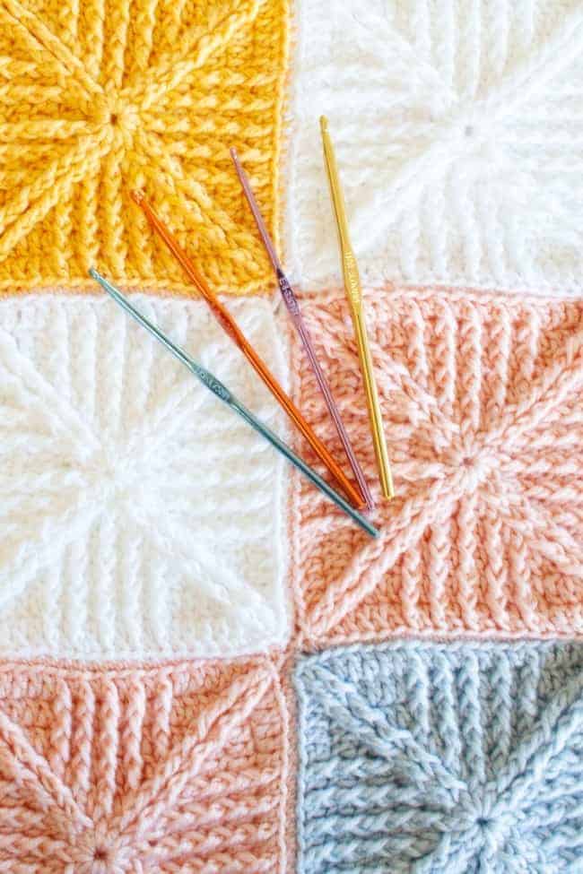four crochet hooks on top of close up of crochet squares baby blanket