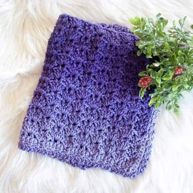 crochet security blanket in purple ombre yarn folded up with greenery