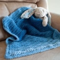 stuffed rabbit holding crochet blanket in blue ombre yarn
