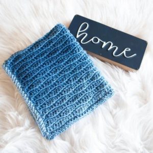 folded blue crochet blanket next to sign saying home