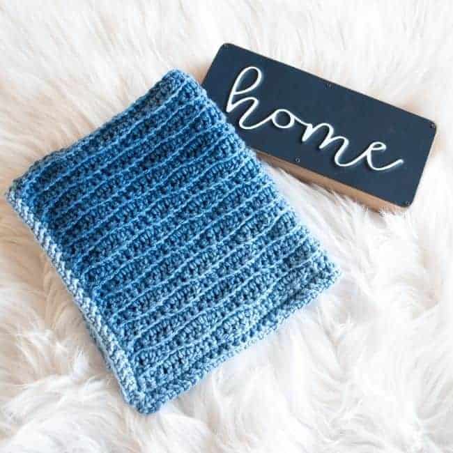 folded blue crochet blanket next to sign that says home all on a white rug