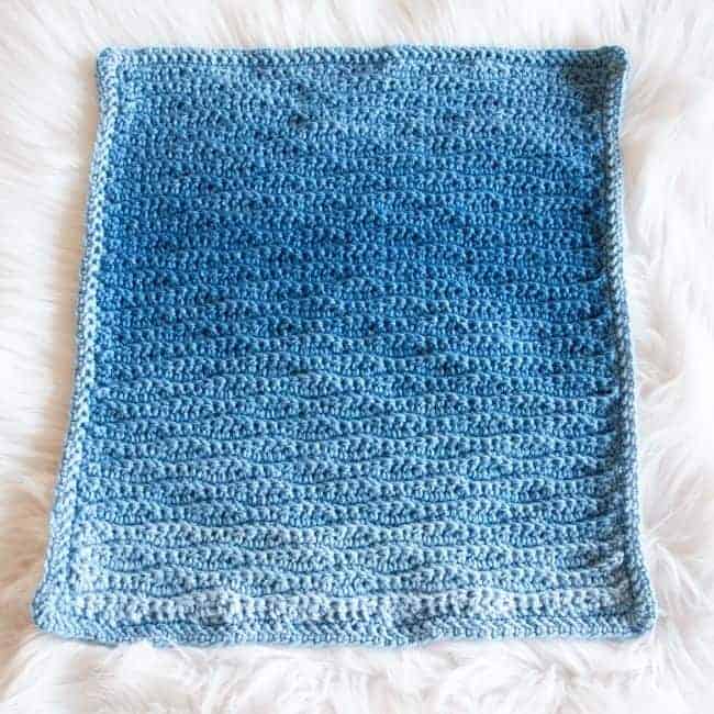 blue ombre crochet blanket laying flat on a white rug