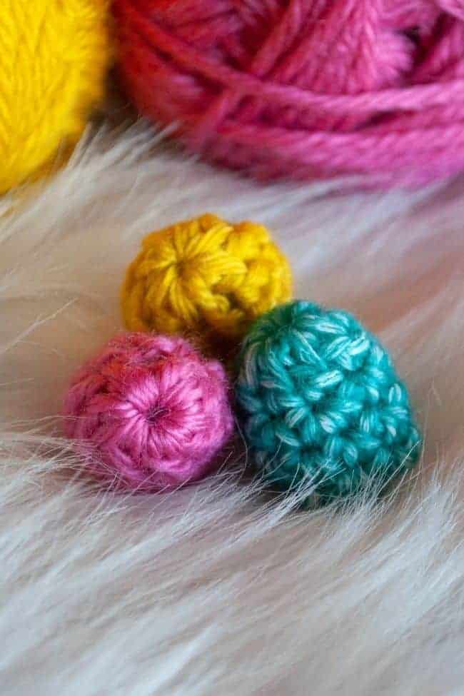 three mini crochet easter eggs in pink, green and yellow with pink and yellow yarn in the background