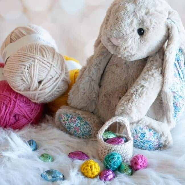 stuffed bunny next to balls of yarn near a mini crochet easter basket and chocolate and mini crochet easter eggs