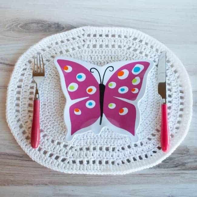 white crochet oval placemat with pink fork knife and butterfly plate on top