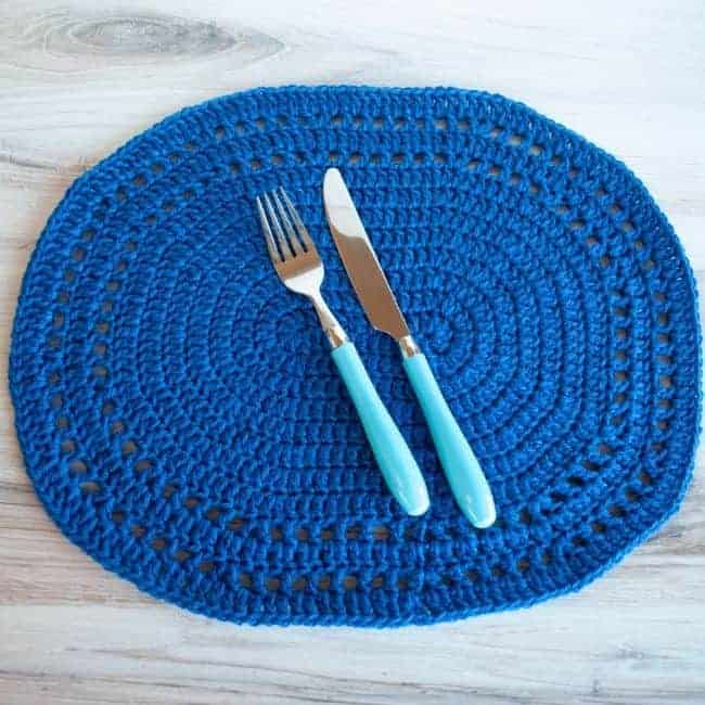 blue crochet oval placemat with blue handled fork and knife on top