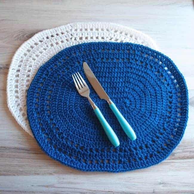 white and blue crochet oval placemats with blue handled fork and knife on top