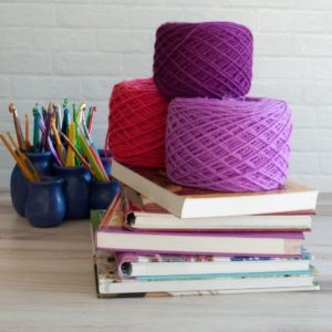 stack of crochet stitches dictionary plus balls of yarn and container full of crochet hooks
