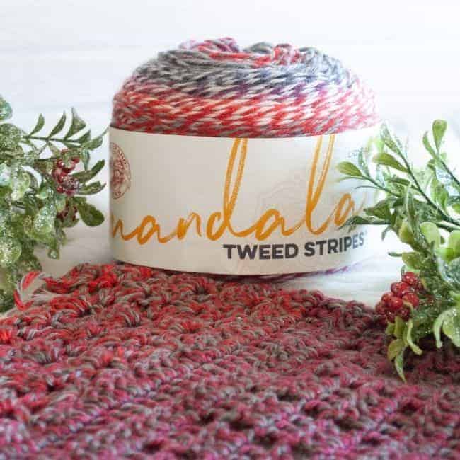ball of mandala tweed stripes yarn, part of scarf, and greenery