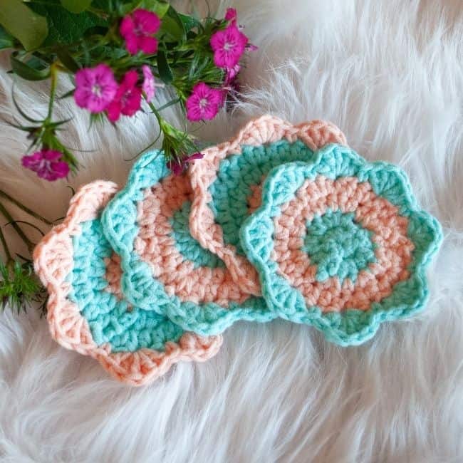 four crochet coasters next to flowers