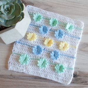 crochet square with flowers on it next to a plant