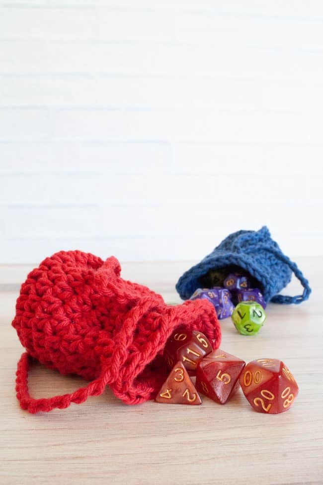 close up of red crochet dice bag with dice spilling out and blue dice bag in background