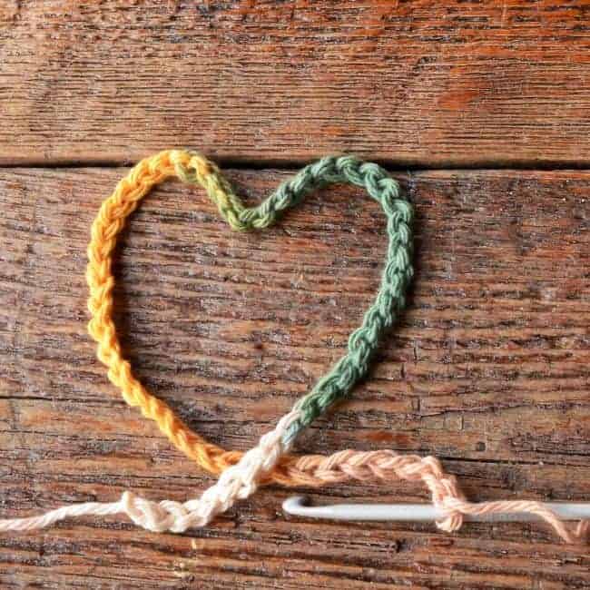 a heart made out of a multicolored crochet chain and a hook