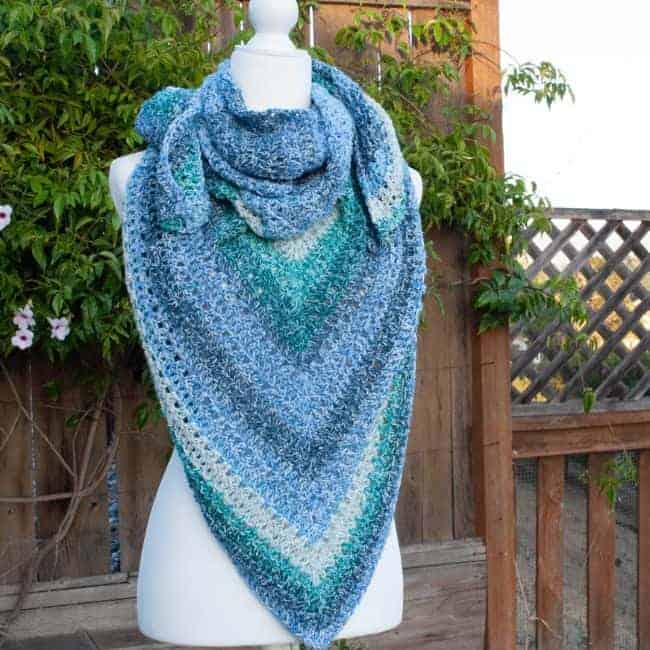 crochet triangle shawl on a mannequin in front of a fence