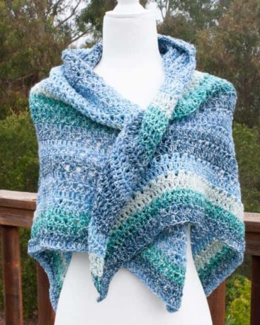 triangle crochet shawl on a mannequin in front of a fence