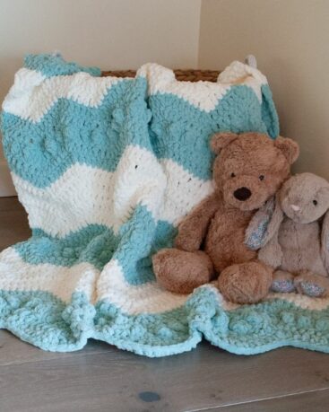 crochet chevron baby blanket draped over a basket with stuffed animals