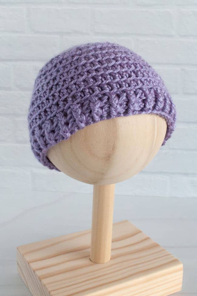 purple crocheted baby hat on a wooden stand