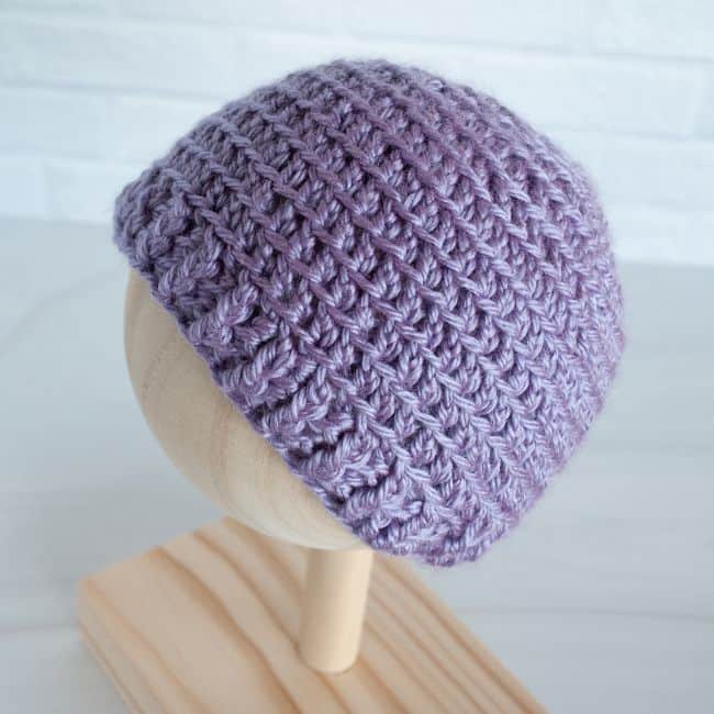 purple crochet baby hat side view on a wooden stand