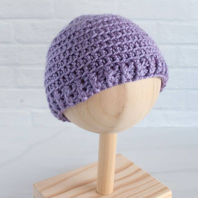 purple crochet baby hat on a wooden stand