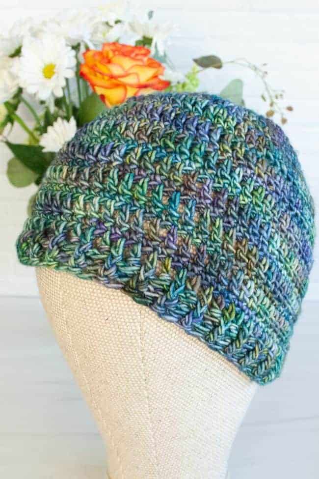 crocheted beanie on a mannequin head with flowers in the background